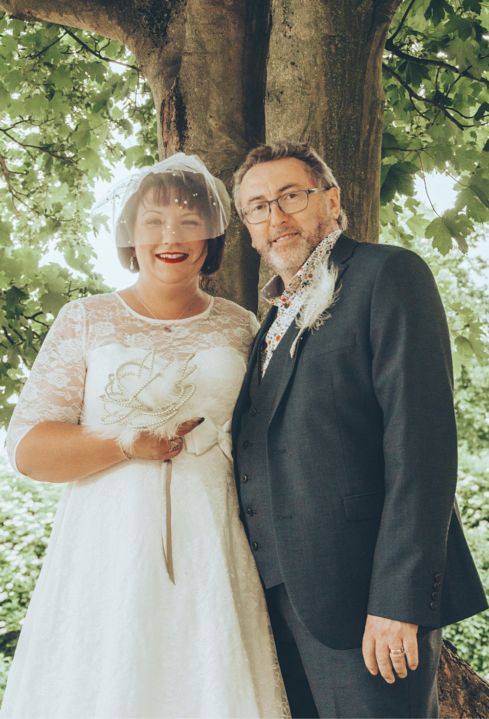 A charming lady in a Madeline Ivory White Dress stands beside her husband