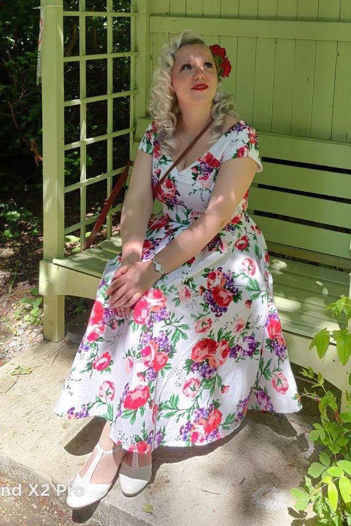 A model wearing a Lily White Floral Off Shoulder Dress is sitting in her garden