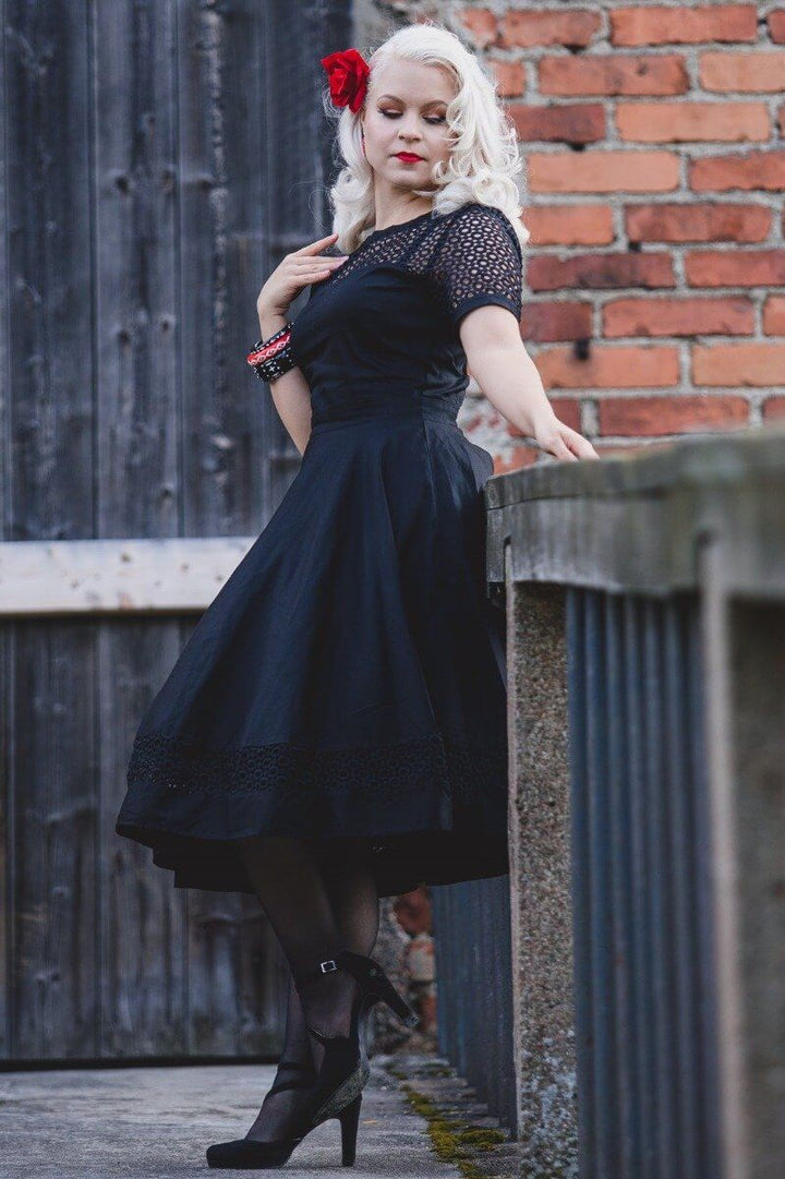 A side angle of A model in a Tess Crochet Lace Formal Dress In Black